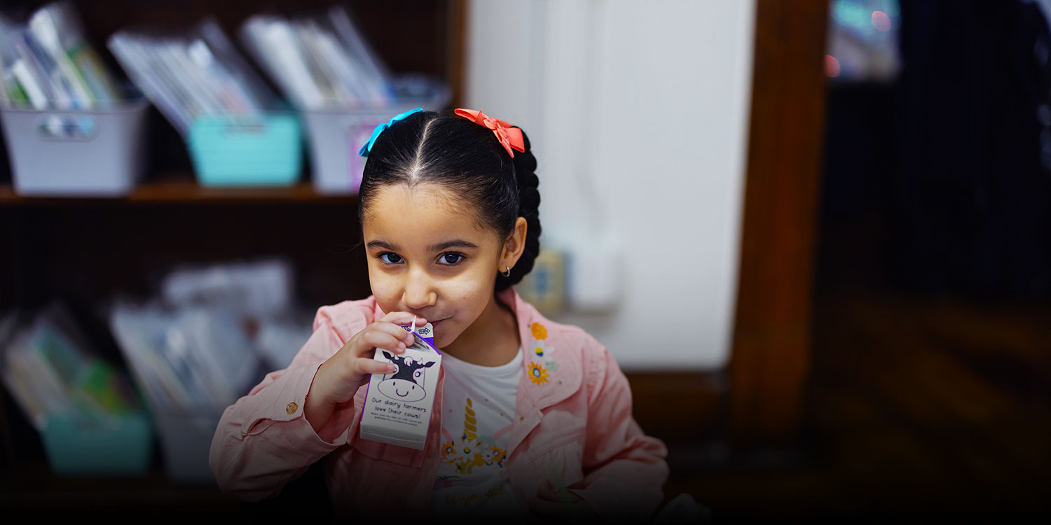 Elementary student eating a meal and drinking from a milk carton.